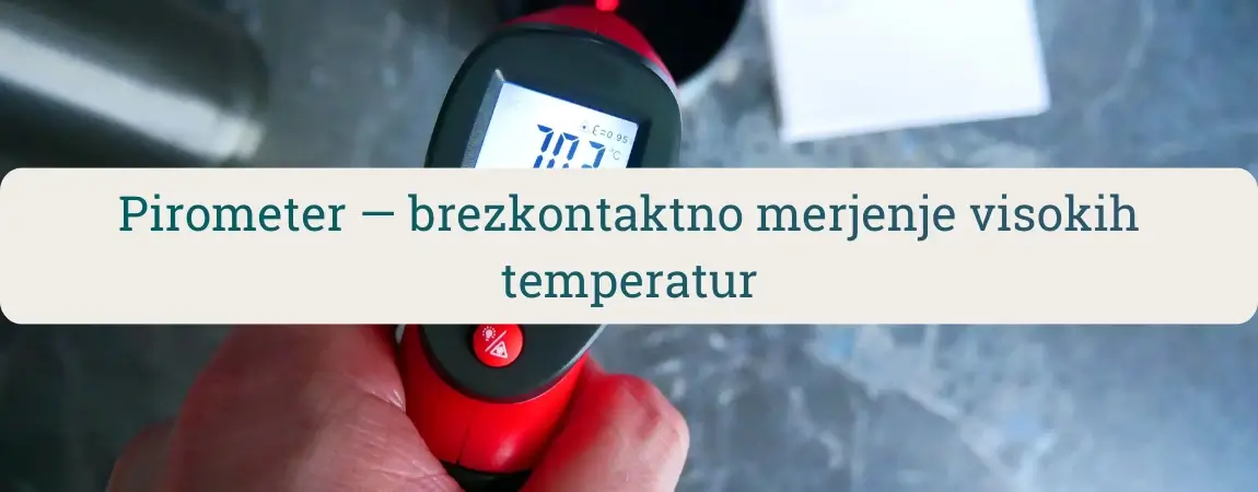 Roka drži rdeč pirometer (IR termometer) in brezkontaktno meri temperaturo površine na delovni mizi.